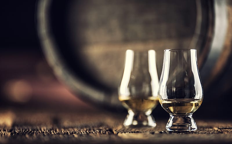 Two GLencairn glasses sitting on floor next to a whiskey barrel. Join the Windows Whiskey Club.