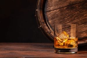 Whiskey with ice next to a barrel