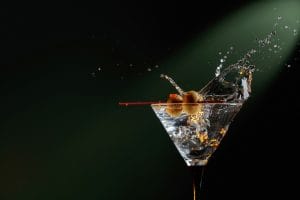 Dry martini with green olives splashing into a glass.